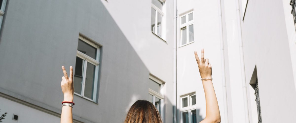 vista-posterior-de-una-mujer-haciendo-gesto-de-paz-cerca-del-edificio