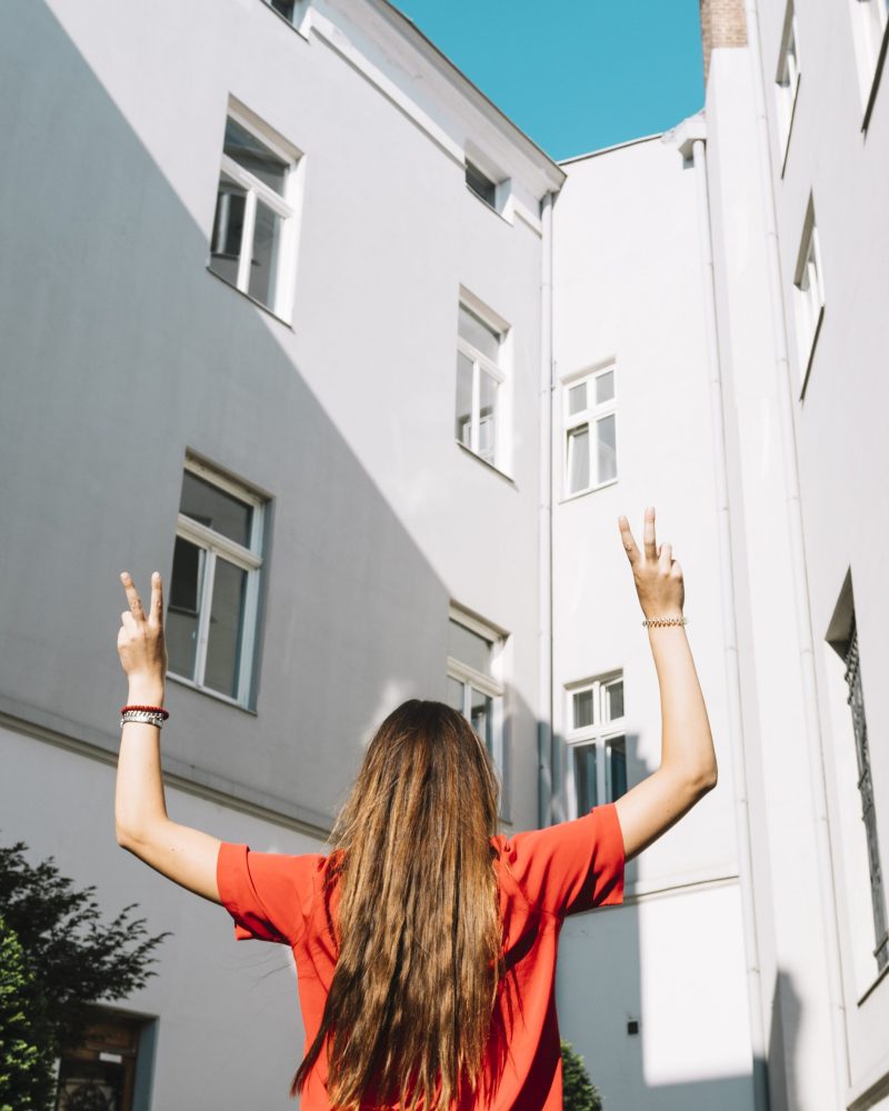 vista-posterior-de-una-mujer-haciendo-gesto-de-paz-cerca-del-edificio